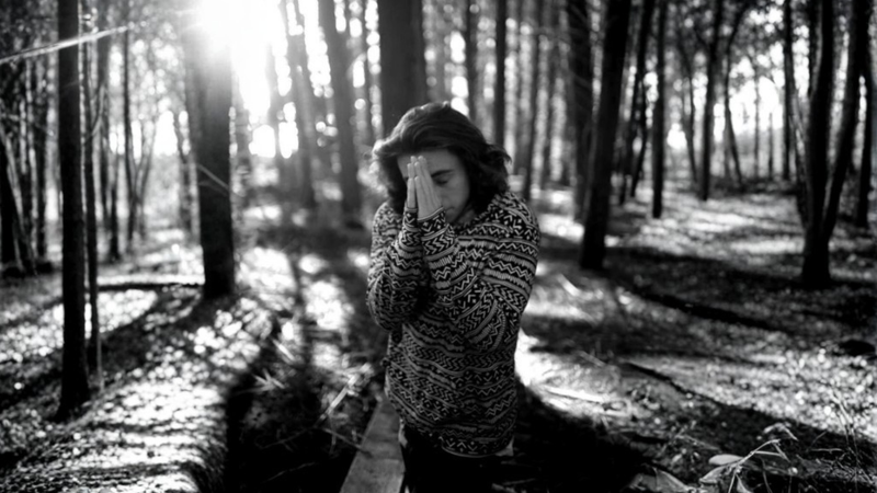 Black and white photo of Harrison kneeling in a sunlit forest with his hands covering his face, representing grief, loss, and the journey toward healing — featured on Lighthouse Lane Books blog.