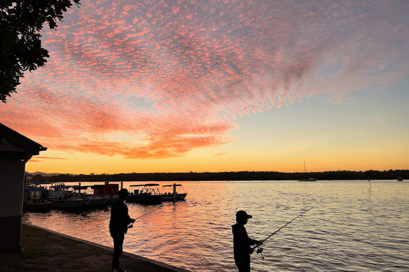 Peaceful sunset scene with silhouetted figures fishing by calm water, symbolizing life's moments of beauty amid suffering and pleasure.